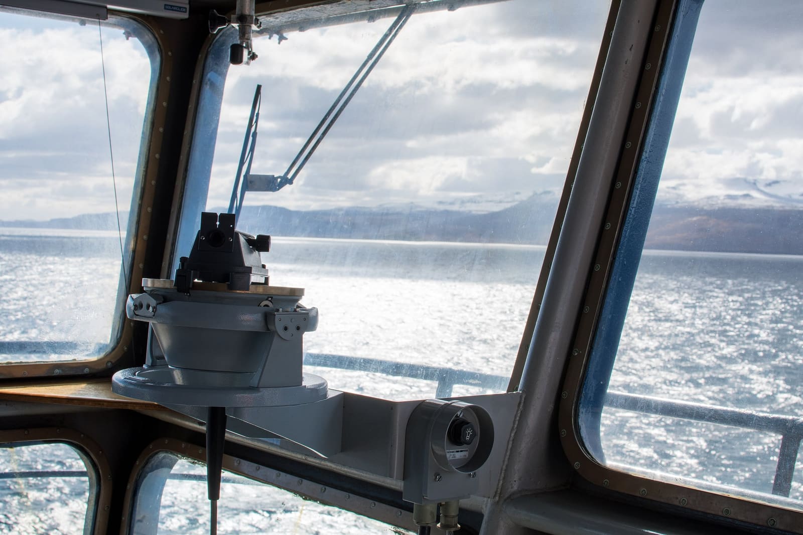Utsikten fra et brovindu: blank sjø, fjell i horisonten og en lyskaster ved rekka.