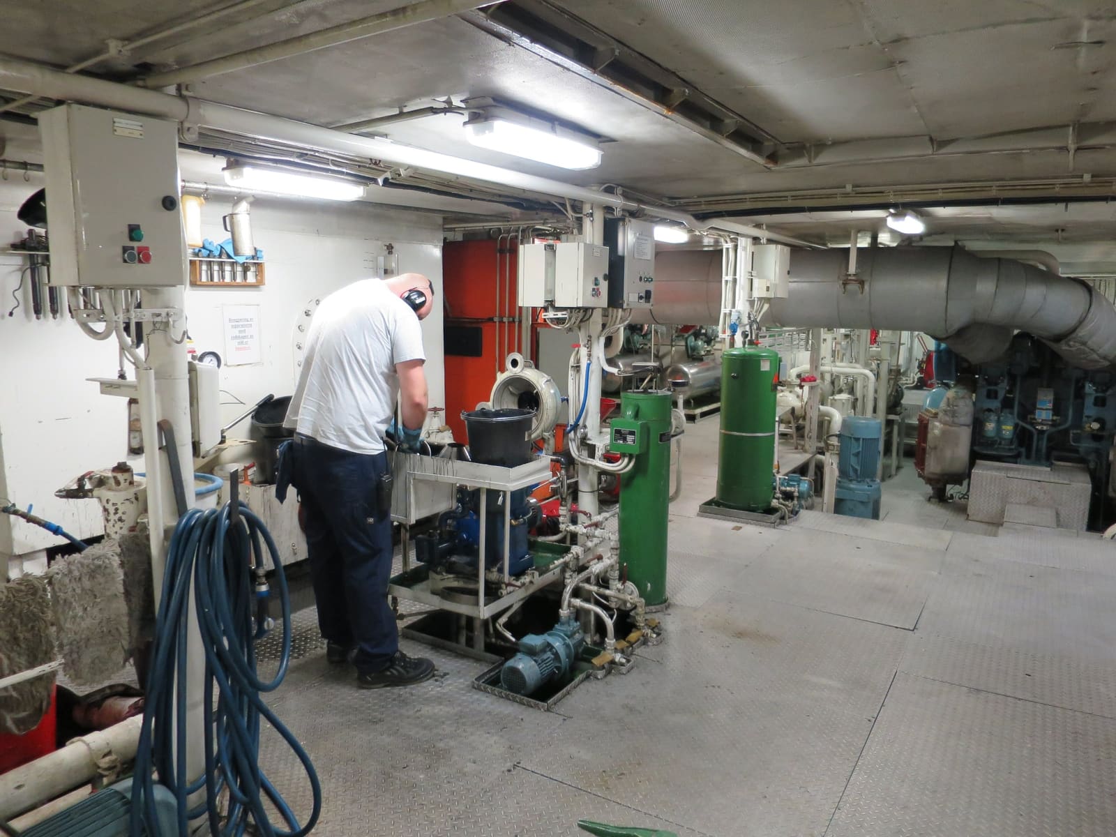 En maskinist som arbeider ved en separator i et maskinrom, blant pumper, tanker og slanger.