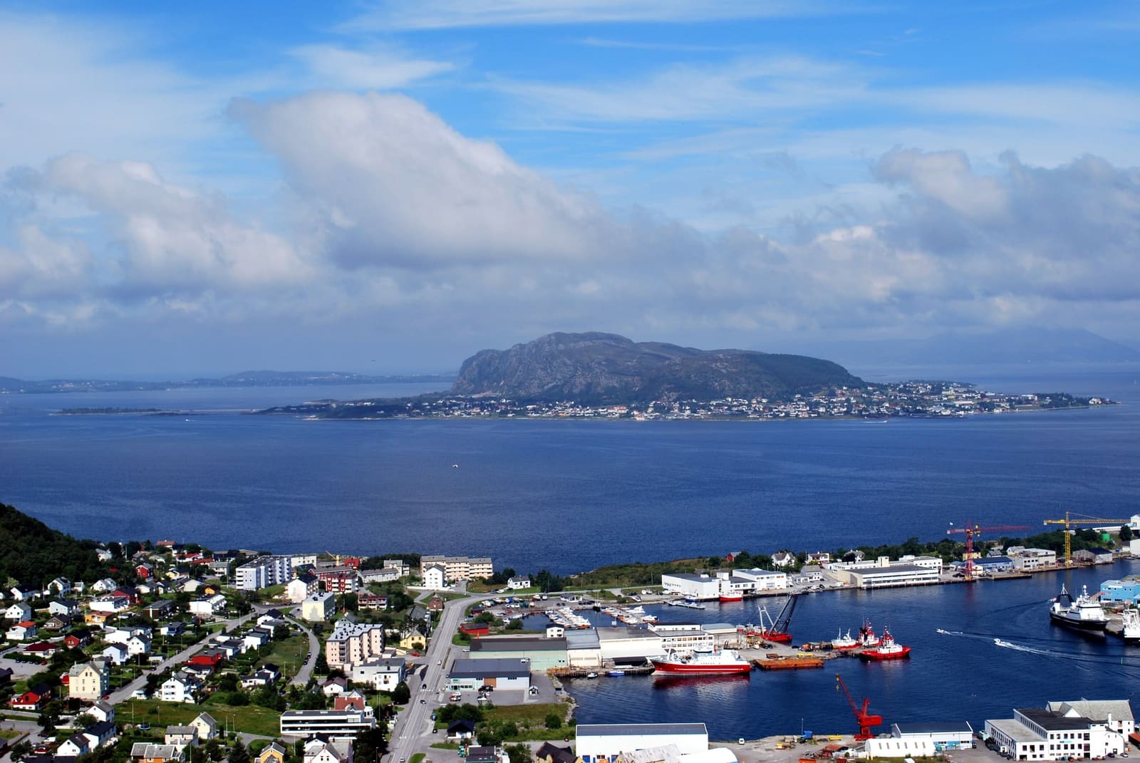 Kysten utenfor Ålesund ovenfra: hus og havn på Valderøya, og Godøya som reiser seg av havet bak.